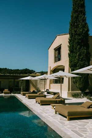 C&acirc;lin poolside terrace with cushioned loungers, white parasols and a tall cypress beside the stone guest house