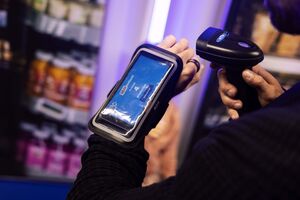Player with a wrist-mounted phone showing their scan score, aiming a hand scanner at a shelf