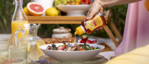 Hand drizzling Meli honey from a squeeze bottle over a summer salad on a sunny garden table